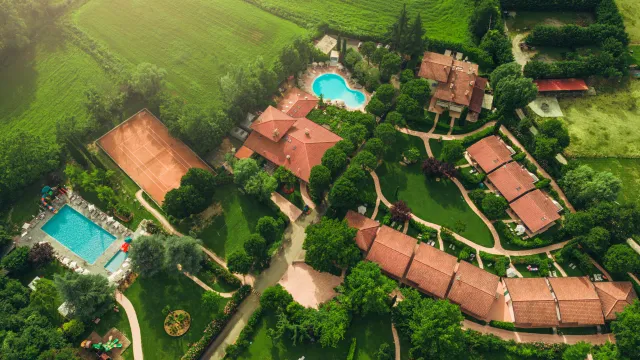 Aerial view of a large estate with lush greenery, red-roofed buildings, and two swimming pools.