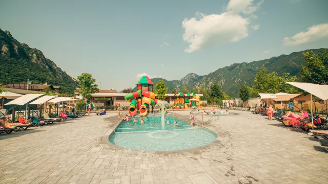 Outdoor pool with colorful slides, surrounded by mountains and loungers.