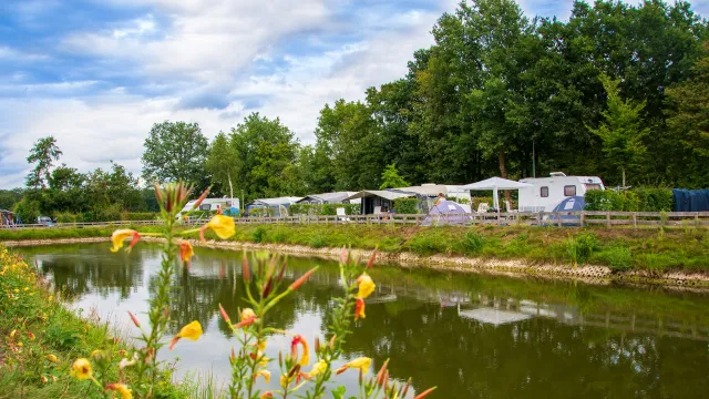 Riverside campground with tents and caravans under a cloudy sky.