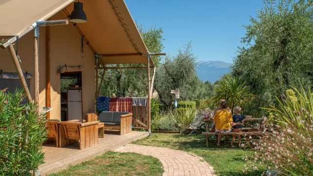 Tent with outdoor seating, people dining nearby, greenery, and mountains in the background.