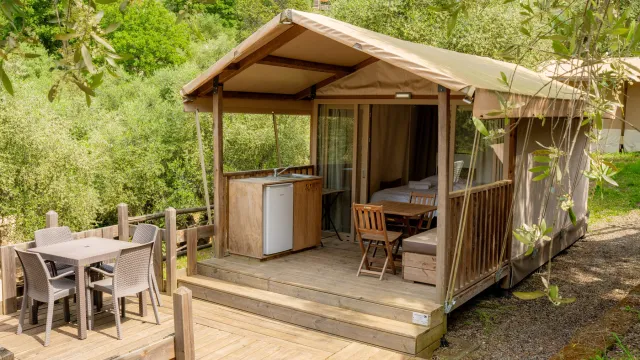Safari-style tent with deck, table, and chairs in a lush outdoor setting.