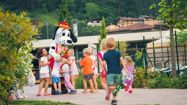 Children gather around a Dalmatian mascot in a park setting.