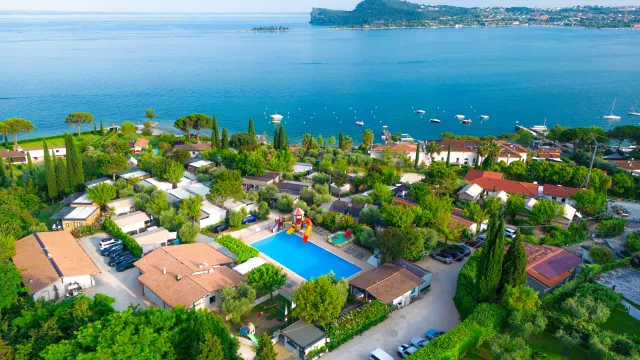 Aerial view of a coastal village with pool, surrounded by greenery and blue sea.