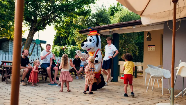 Children interacting with a costumed character outdoors, sunny day.