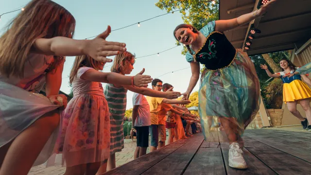Children and adults high-fiving on a wooden stage at sunset.
