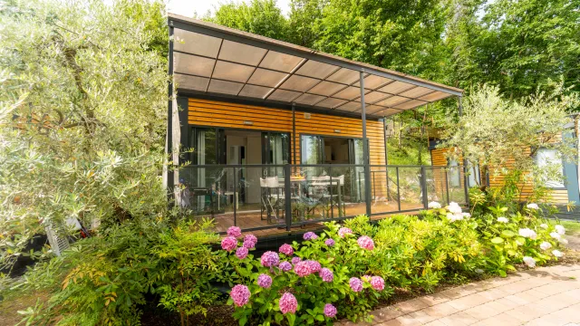 Modern house with large patio, surrounded by lush greenery and blooming flowers.