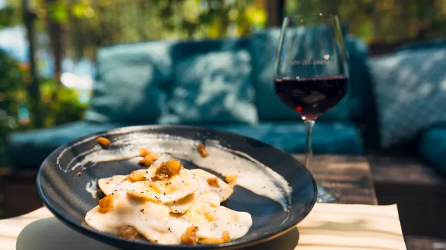 Dish of ravioli with creamy sauce, accompanied by a glass of red wine on a sunny patio.