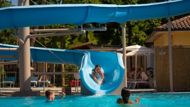 Child slides down blue water slide into a pool with other children swimming.