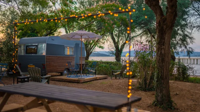Camper van by a lake, surrounded by trees and string lights.