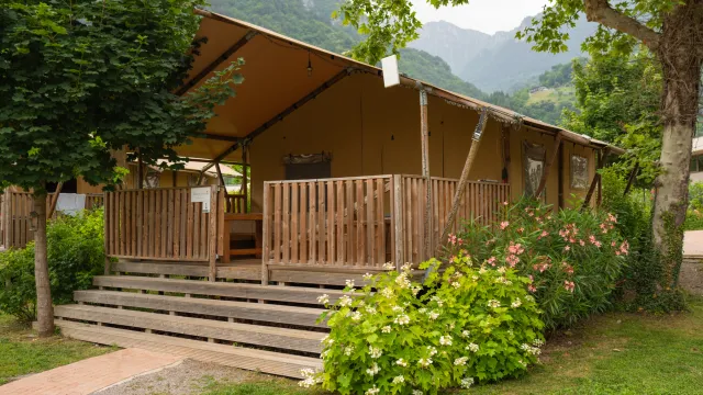 Wooden cabin with porch, surrounded by greenery and mountains.
