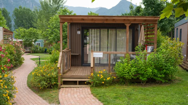 Small wooden cabin with a porch, surrounded by greenery and a winding brick path.