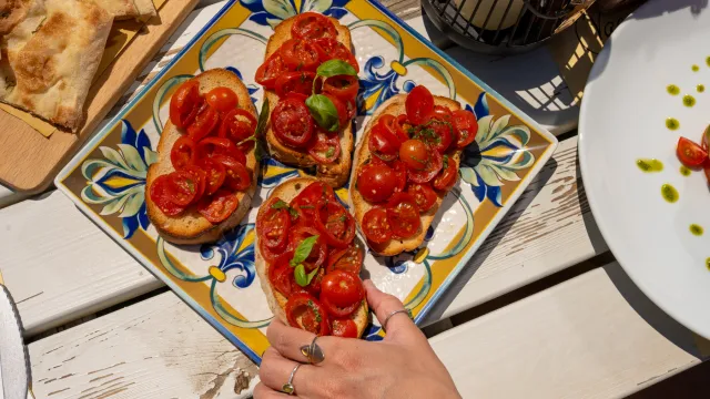 Bruschetta with tomatoes on a colorful plate, a hand reaching for a piece.