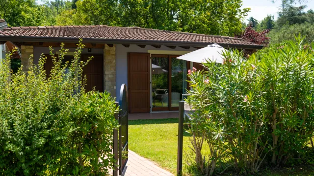 House with wooden doors, lush garden, and sun umbrella on a sunny day.