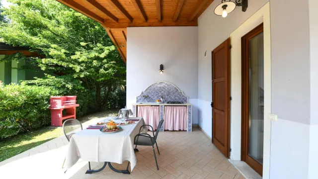 Covered patio with table, chairs, and outdoor kitchen surrounded by greenery.