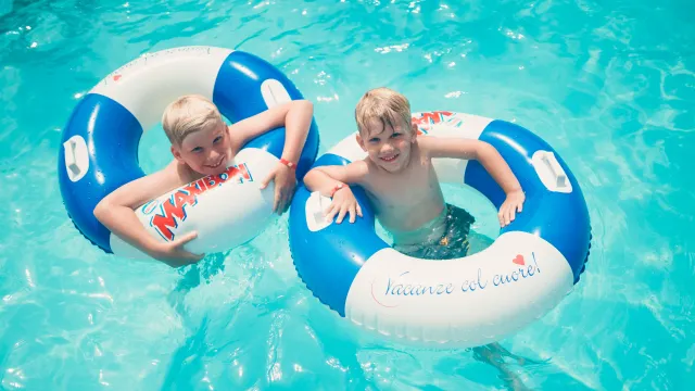 Two children smiling in pool with blue and white float rings.