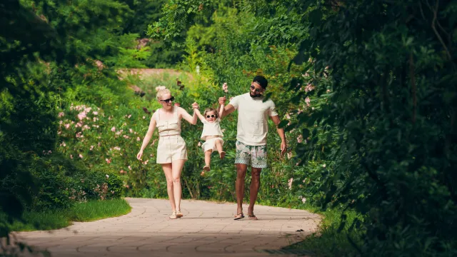 Family walking on a lush green path, swinging a child between them.
