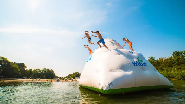 Teens jumping off an inflatable iceberg in a sunny lake.