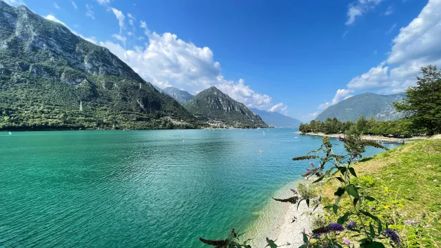 Mountainous lake landscape under a bright blue sky with fluffy clouds.