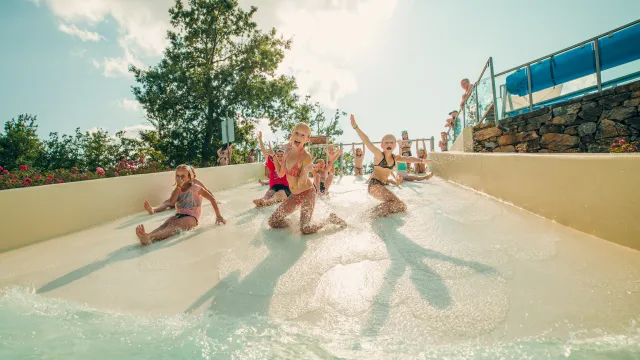 Children sliding down a water slide on a sunny day, splashing and smiling.