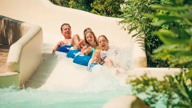 Family sliding down a water slide with joyful expressions and splashing water.