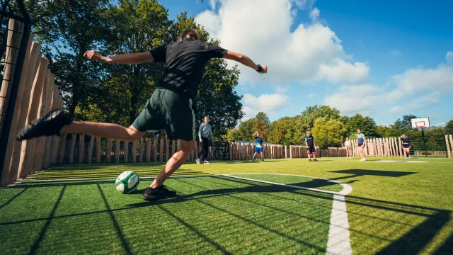 Soccer player kicking a ball on a sunny outdoor field.