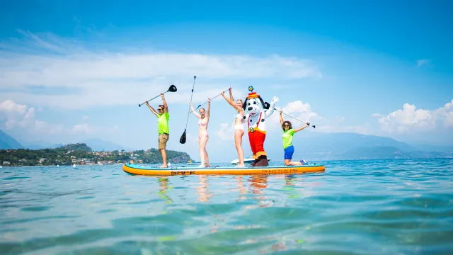 Four people in bright shirts paddleboarding on clear blue water under a cloudless sky.