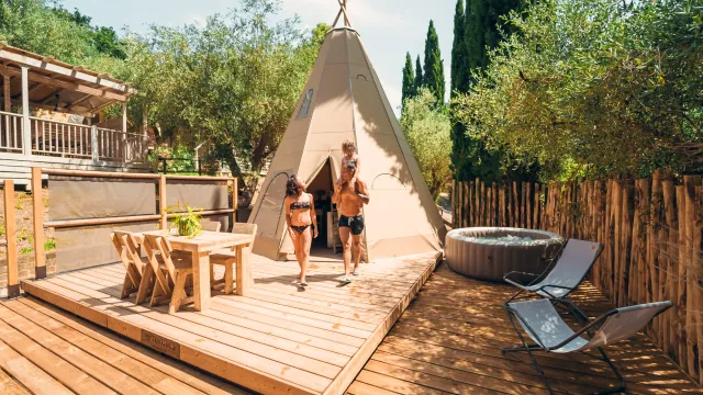 Couple exiting a tipi on a wooden deck with hot tub and chairs nearby.