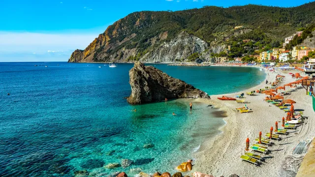 Beach with turquoise water, colorful umbrellas, and rocky cliffs under a clear blue sky.