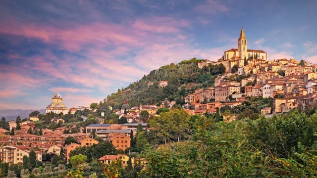 Hilltop town with sunset sky, lush greenery, and rustic buildings.