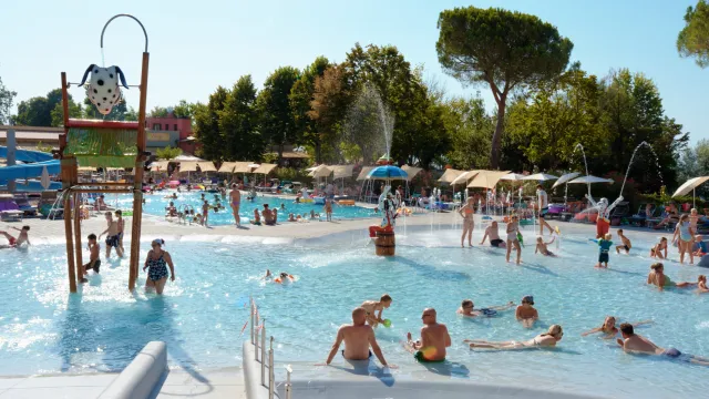 Crowded outdoor pool with people swimming and relaxing under a sunny sky.