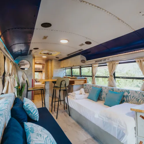 Converted bus interior with blue accents, couches, and a small dining area.