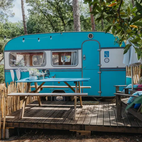 Teal caravan on a wooden deck surrounded by trees.