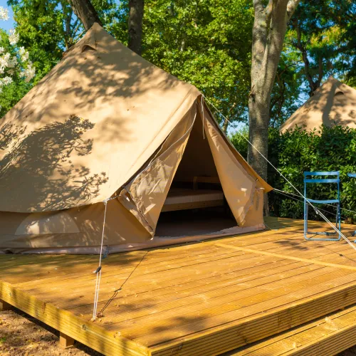 Tent on wooden platform surrounded by trees, with two blue folding chairs.