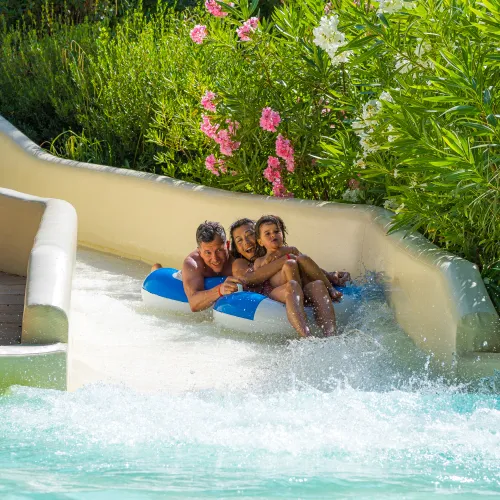 Three people in an inflatable raft slide down a water slide.