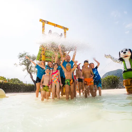 Children playing in a water park, splashing under a large bucket.