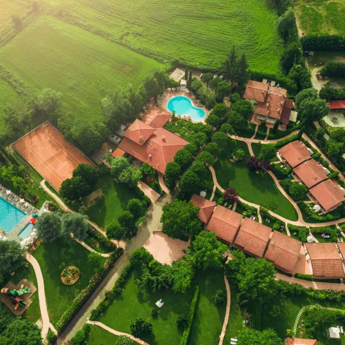Aerial view of resort with two pools, surrounded by green fields and trees.