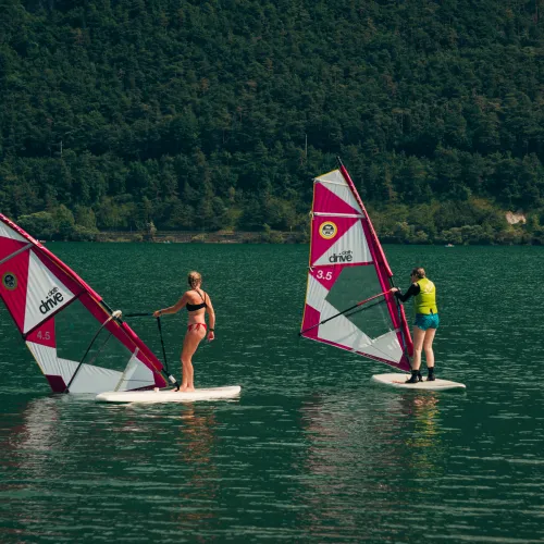 Windsurfers on a lake with forested hills in the background.
