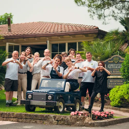 Group posing in front of a building, some making hand signs, small vehicle in foreground.