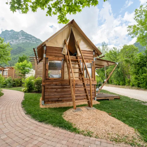 Cabin with canvas roof, surrounded by trees, mountains in the background.