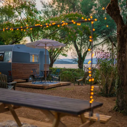 Campervan by a lake with string lights and trees at sunset.