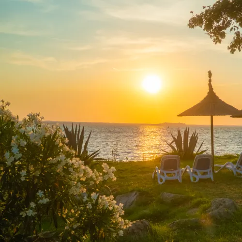Tropical sunset over the lake with lounge chairs and parasols on the grassy shore.