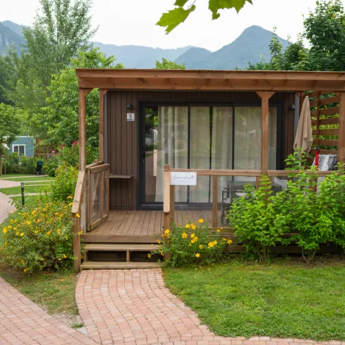 Small wooden cabin with a porch, surrounded by greenery and a winding brick path.
