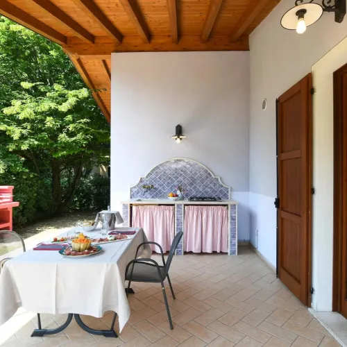 Covered patio with table, chairs, and outdoor kitchen surrounded by greenery.