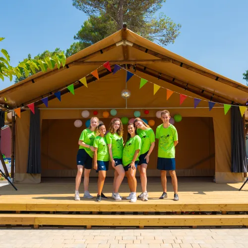 Group of kids in green shirts on a wooden stage under a sunny sky.