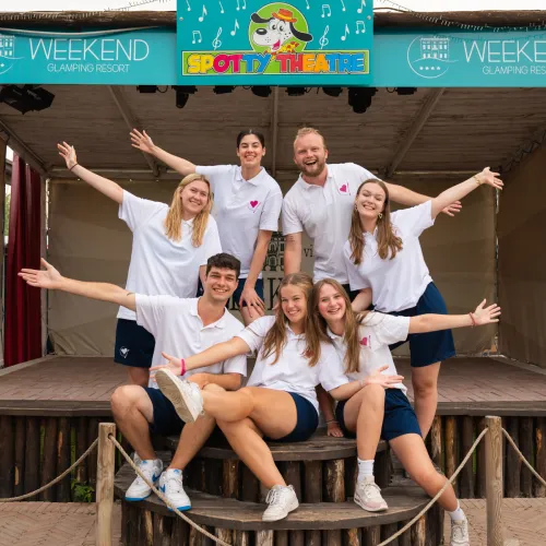 Seven people in matching shirts pose cheerfully on a stage.
