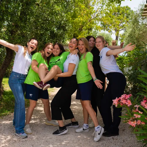 Group of smiling women posing outdoors surrounded by greenery.