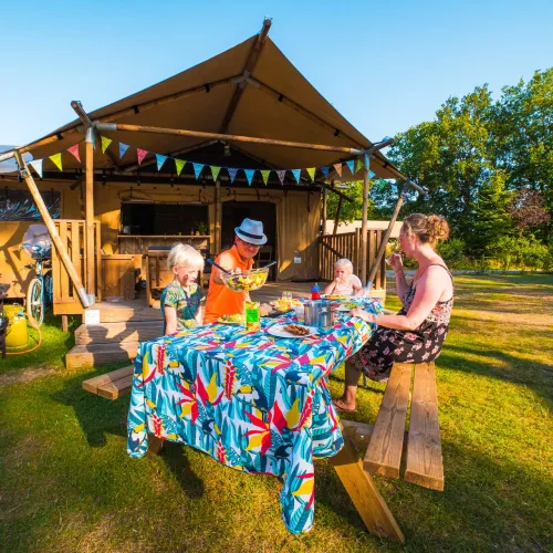 Family enjoying a picnic at a colorful table outside a wooden hut.