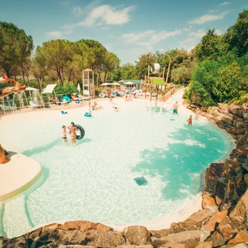 Tropical pool with people swimming, surrounded by trees and rocks.
