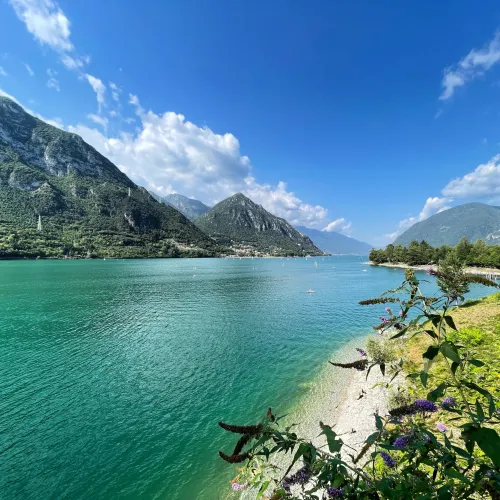 Mountainous lake landscape under a bright blue sky with fluffy clouds.