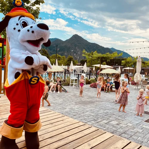 Spotty in red pants on stage, mountains and crowd in background.